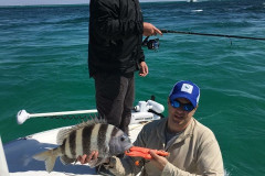 one man holding a fishing pole next to a nealing man holding a caught grouper